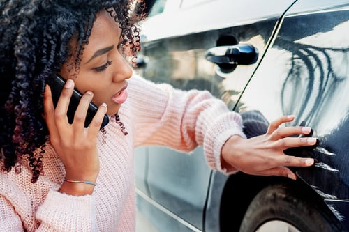 Woman on cell phone examining car scratches woman on cell phone examining scratches on car