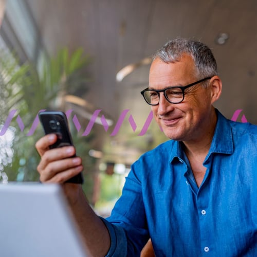 Photo of a smiling, casually dressed man reading something on his cellphone. In the background, a series of small purple wave forms run across the frame, representing communications.