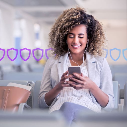 Fraud Defender image Photo illustration of a woman with a cell phone in her hands and wearing headphones; behind her are a row of security badges in purple and blue superimposed onto the background of the photo indicating security measures