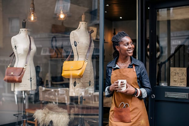 business owner standing outside shop business owner standing outside fashion shop holding cup of coffee